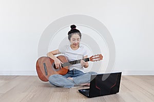 Young Asian woman play guitar, with computer laptop in living room