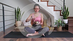 Young Asian woman playing Tibetan singing bowl sitting in meditation at home. 4k resolution.