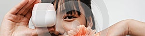 Young asian woman posing with face cream and gerbera flower