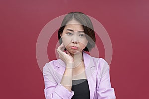 A young asian woman pouts while having a throbbing toothache, looking pitiful. Studio shot with burgundy background