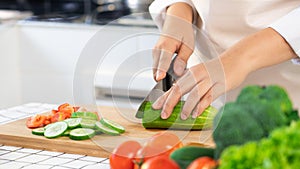 Young Asian woman is preparing healthy food vegetable salad by Cutting cucumber for ingredients on cutting board on light kitchen