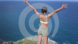 Young Asian woman raising hands outstretched and standing on cliff of the mountain in a sea view