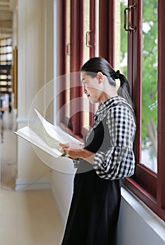 Young asian woman reading book near windows in the library
