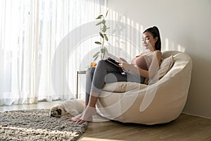 Young asian woman reading book with pug dog in living room at home