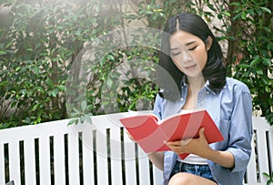 Young Asian woman reading a book relaxing in chair at garden on