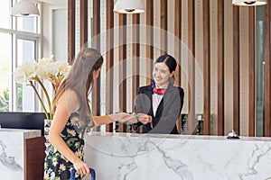 Young Asian woman receptionist at the hotel counter talking with blurred female travelers check-in at the hotel, Female