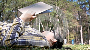 Young Asian woman relaxation and reading a book lying on grass in the garden on vacation day.