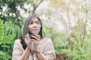 Young Asian woman relaxing at garden with a cup of coffee in a morning. A woman inhaled coffee