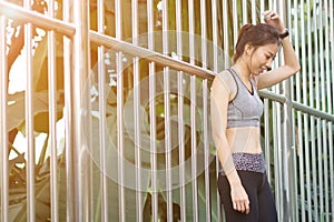 Young asian woman relaxing after jogging exercise stand against steel in park to freshen her body and enjoy warm light in morning. photo