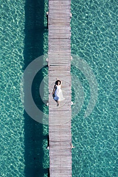 Young asian woman relaxing on wooden pier in tropical sea on summer vacation
