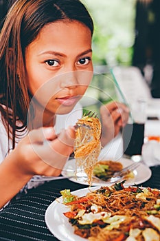 Young Asian woman at the restaurant eating stir fry rice noodle with meat and vegetables, Philippine food call pansit bihon