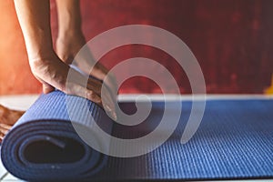 Young asian woman rolling blue yoga mat or fitness mat in livingroom, Healthy concept, Mind-body improvements concept