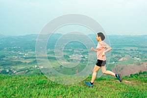 Young Asian woman runner, wearing black sportswear, running on a big mountain trail, cool morning, windmills, and sky in the