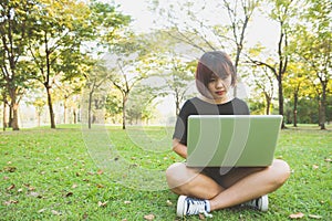 Young asian woman`s legs on the green grass with open laptop. Girl`s hands on keyboard.