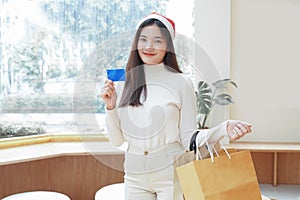 Young Asian woman in santa hat with shopping bags and Credit Card in her hand at shopping mall