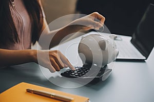 Young Asian woman saving for retirement Saving money through a piggy bank and taking notes on notebook, savings concept