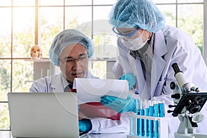 Woman and senior man researcher scientist with laptop, lab coat, gloves and eyeglasses analyzing experiment together