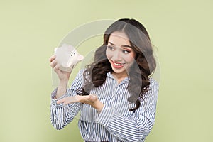 Young asian woman shaking out empty piggy bank on green background.