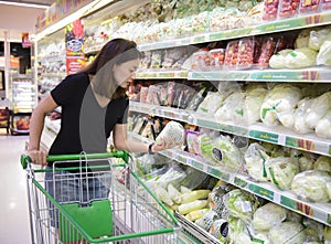 Young asian woman with shopping cart choosing products in supermarket