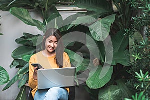 Young Asian woman shopping online with her laptop in a coffee shop garden.