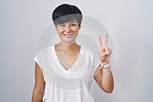 Young asian woman with short hair standing over isolated background showing and pointing up with fingers number two while smiling