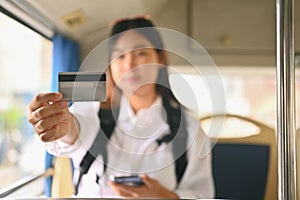 Young Asian woman showing credit card while sitting inside public bus transport