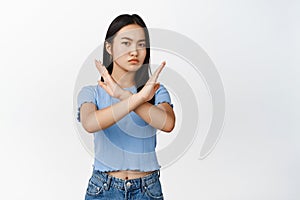 Young asian woman shows cross, stop block gesture, tell no, prohibit something bad, frowning displeased, standing over