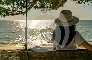 Young Asian woman sit and relax on swings at seaside on summer vacation. Summer vibes. Woman travel alone on holiday. Backpacker