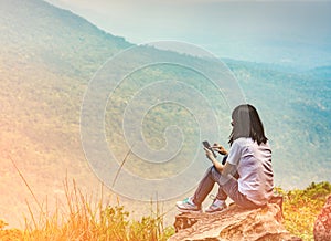 Young Asian woman sit on the rock at the cliff and using smart phone message to her friends while on vacation at the national park