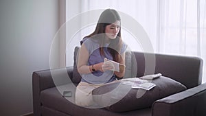 Young asian woman sit on sofa using a calculator to calculate income and expenses or managing monthly budget