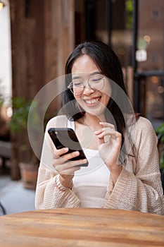 A young Asian woman sits at an outdoor table of a cafe and uses her phone to read something online