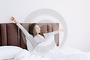 Young asian woman sitting on the bed and stretch oneself