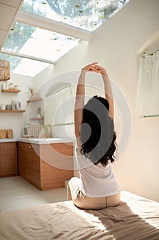 Young asian woman sitting on the bed and stretch oneself in the morning at home