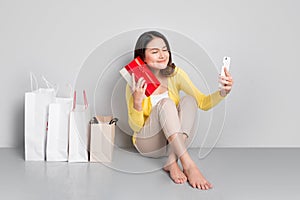 Young asian woman sitting besides row of shopping bags holding r