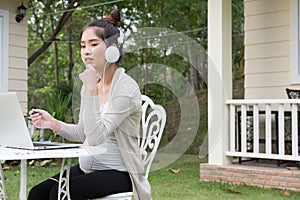 Young asian woman sitting on chair listening to music and using