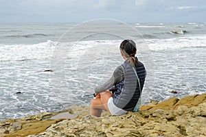 Young Asian woman sitting on a cliff and looking far away at the sea