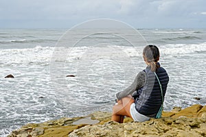 Young Asian woman sitting on a cliff and looking far away at the sea