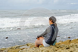 Young Asian woman sitting on a cliff and looking far away at the sea