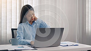 Young asian woman is sitting in a corporate office and has pain in her neck