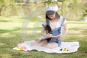 Young asian woman sitting drawing picture with colorful paint brush while leisure in the park on summer.