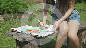 Young asian woman sitting drawing picture with colorful paint brush while leisure in the park on summer.