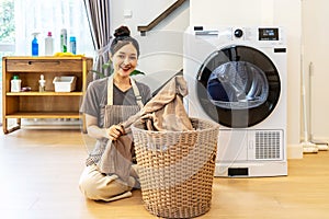 Young asian woman sitting on floor folding clothes at laundry room, girl take clothes from basket and fold it. Concept of washing