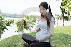 Young asian woman sitting in fresh spring grass listening to mus