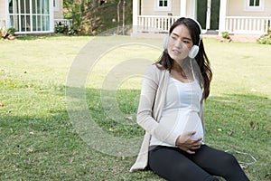 Young asian woman sitting in fresh spring grass listening to mus