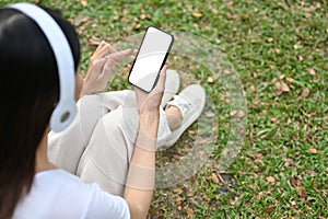 Young Asian woman sitting on grass, wearing headphones, relaxing in the public city park