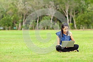 Young asian woman sitting on green grass field using laptop