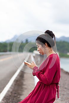 Young asian woman sitting on guard rail and using smartphone