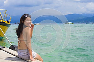 Young Asian woman sitting happy on sea dock at Thailand beach looking at the horizon beautiful marine landscape with mountains enj