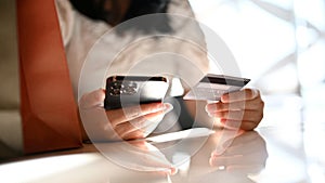 Young Asian woman sitting at her table, holding her smartphone and her credit card. cropped