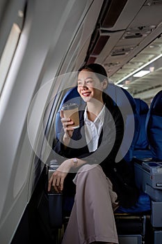 Young Asian woman sitting near the window on a business class airplane during a flight. Travel and business concept.